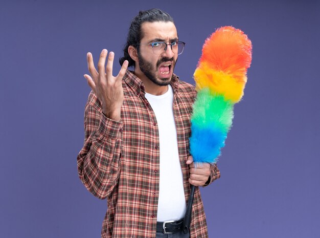 Jeune beau mec de nettoyage en colère portant un t-shirt tenant pipidaster isolé sur un mur bleu avec espace de copie