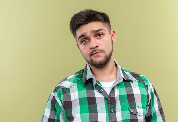 Jeune beau mec portant une chemise à carreaux à la confusion debout sur un mur kaki