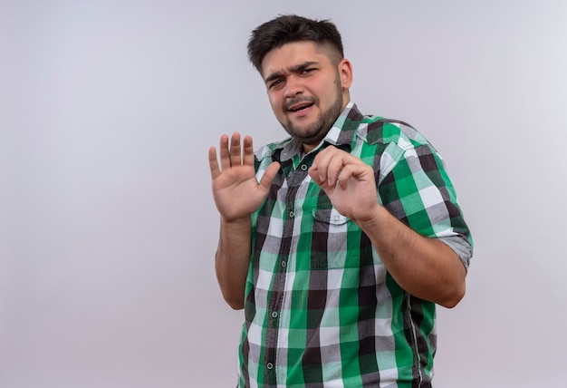 Jeune beau mec portant une chemise à carreaux à la peur debout sur un mur blanc