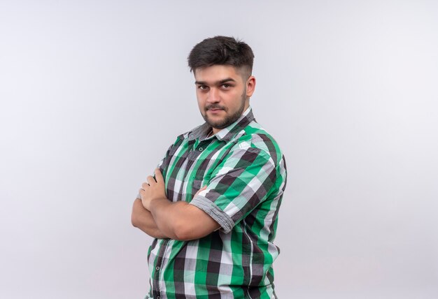 Jeune beau mec portant une chemise à carreaux à la recherche concentrée debout sur un mur blanc