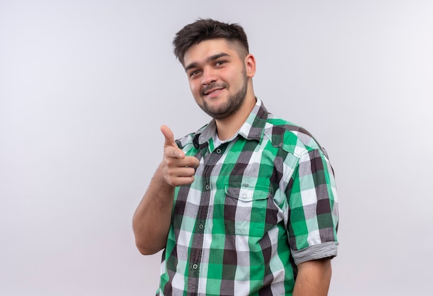 Jeune beau mec portant chemise à carreaux souriant pointant debout sur un mur blanc