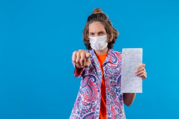 Jeune beau mec portant un masque de protection du visage montrant la carte pointant vers la caméra en colère et furieux avec vous debout sur fond bleu