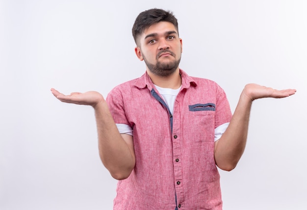 Jeune beau mec portant un polo rose à l'indécis debout sur un mur blanc