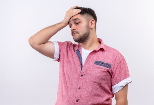 Jeune beau mec portant un polo rose souffrant de maux de tête tenant sa tête avec la main debout sur un mur blanc