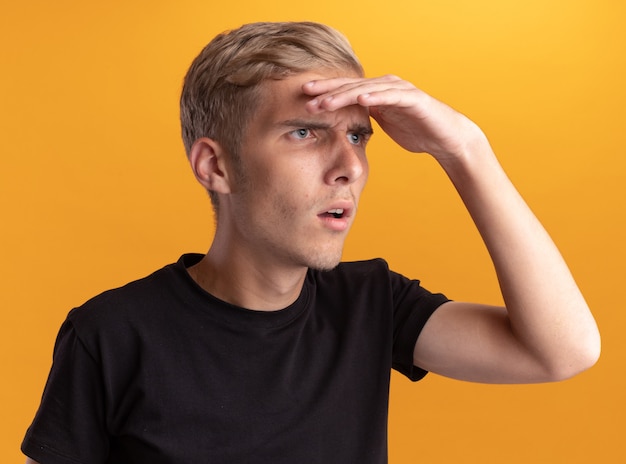 Photo gratuite jeune beau mec vêtu d'une chemise noire regardant la distance avec la main isolée sur le mur jaune