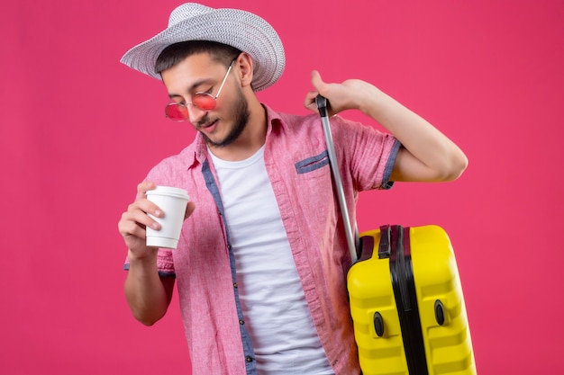 Jeune Beau Mec Voyageur En Chapeau D'été Portant Des Lunettes De Soleil Tenant Valise Et Tasse De Café à La Confiance Debout Sur Fond Rose