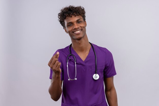 Un jeune beau médecin à la peau sombre avec des cheveux bouclés portant l'uniforme violet avec stéthoscope souriant et