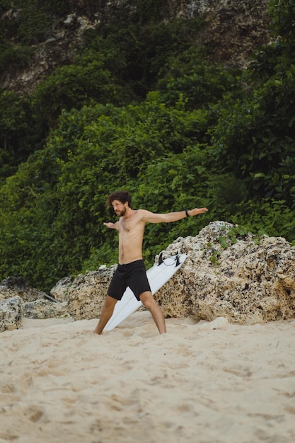 Un jeune et beau surfeur au bord de l'océan fait un échauffement avant de surfer. exercices avant le sport, étirements avant le surf.