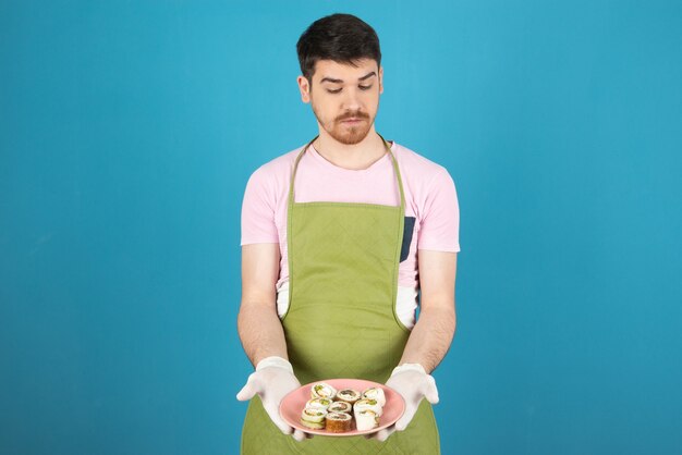 Jeune beau et tenant des rouleaux de gâteau et le regardant.