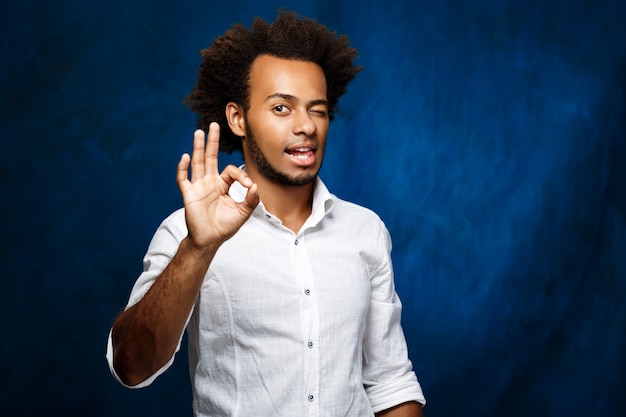 Jeune bel homme africain montrant bien, un clin de œil sur le mur bleu.