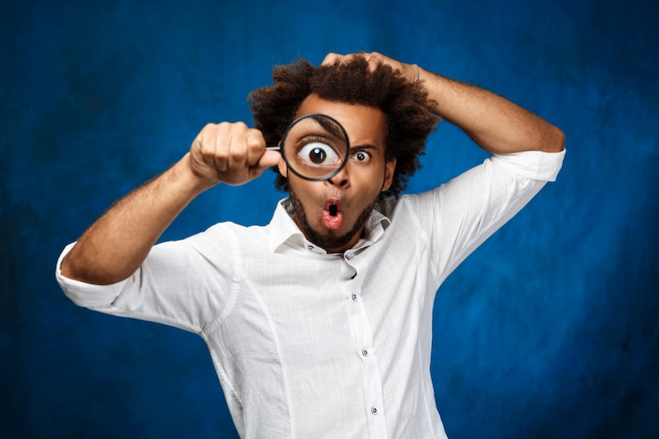 Photo gratuit jeune bel homme africain posant avec loupe sur mur bleu.