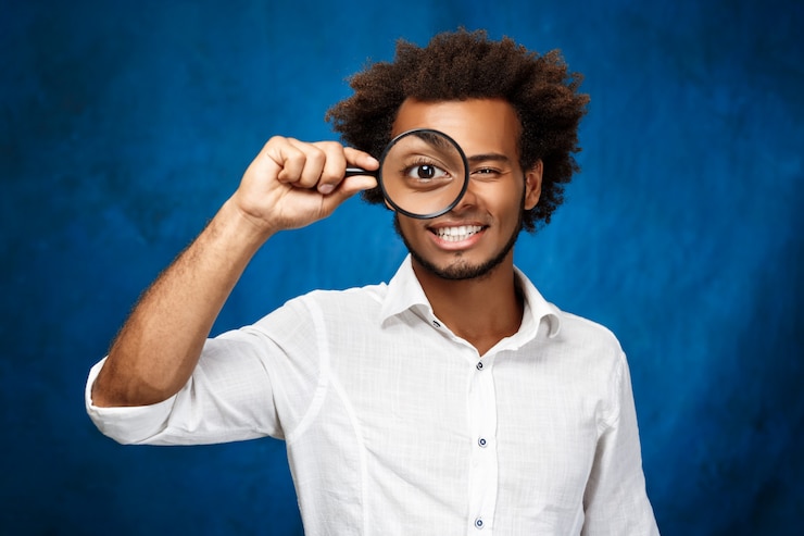 Photo gratuit jeune bel homme africain posant avec loupe sur mur bleu.