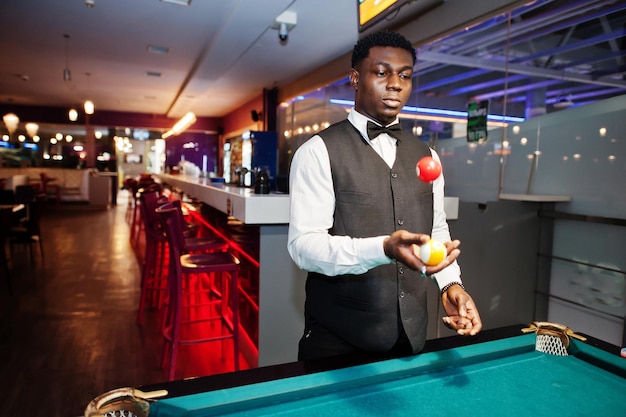 Jeune bel homme africain vêtu d'une chemise blanche, d'un gilet noir et d'un nœud papillon jouer au billard billard