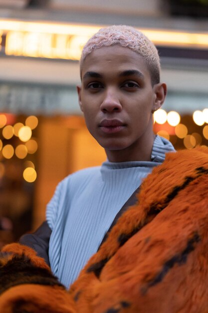 Jeune bel homme afro-américain posant à l'extérieur à Paris. sourire heureux, style de mode. lumières des cafés du soir.