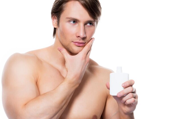 Jeune bel homme appliquant une lotion sur le visage - isolé sur blanc.