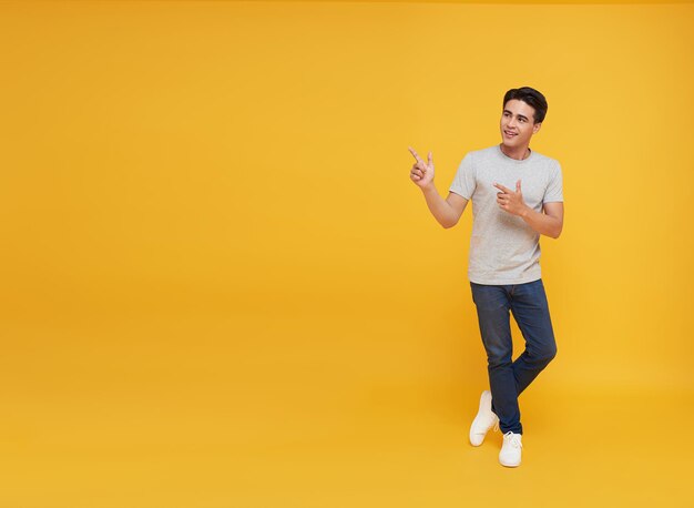 jeune bel homme asiatique pointant du doigt dans un espace vide de côté dans un studio isolé sur fond jaune