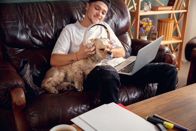 Jeune bel homme assis sur un canapé marron et travaillant avec son chien mignon