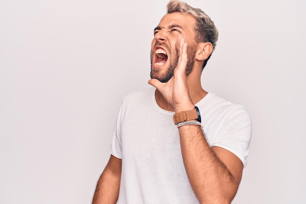 Photo gratuite jeune bel homme blond portant un t-shirt décontracté debout sur fond blanc isolé criant et hurlant fort à côté avec la main sur la bouche concept de communication