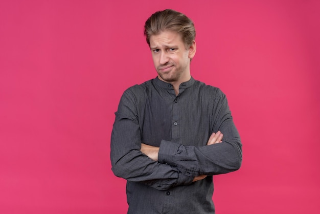 Jeune bel homme avec les bras croisés avec une expression dégoûtée debout sur un mur rose