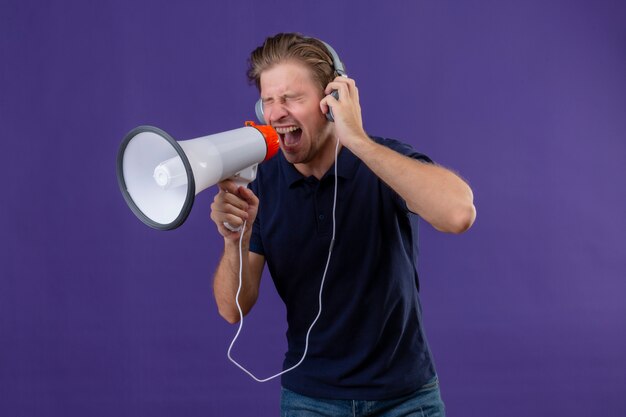 Jeune bel homme avec un casque criant à travers un mégaphone debout sur fond violet