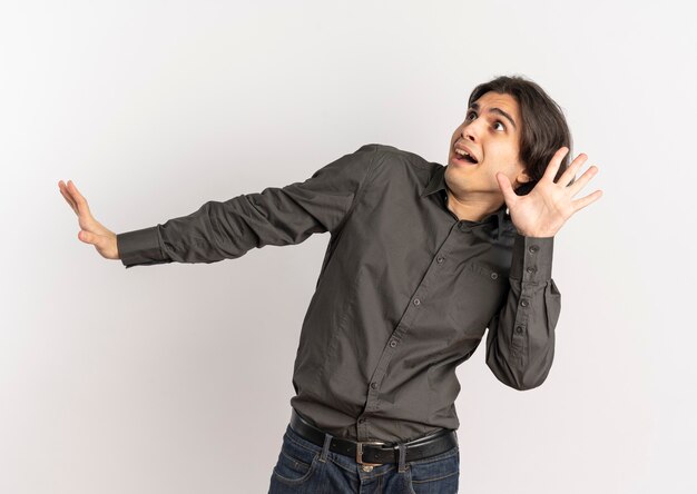 Jeune bel homme caucasien effrayé tient les mains ouvertes et regarde le côté isolé sur fond blanc avec copie espace