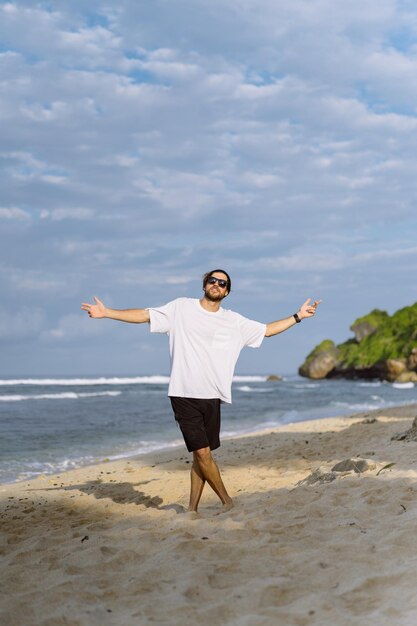 Jeune bel homme avec un charmant sourire en lunettes de soleil sur la plage.