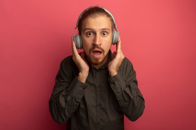 Jeune bel homme en chemise grise avec un casque sur sa tête étonné et surpris