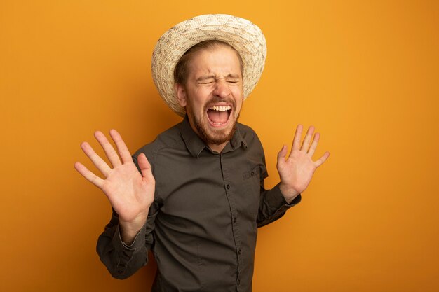 Jeune bel homme en chemise grise et chapeau d'été hapy et excité avec les bras levés en riant