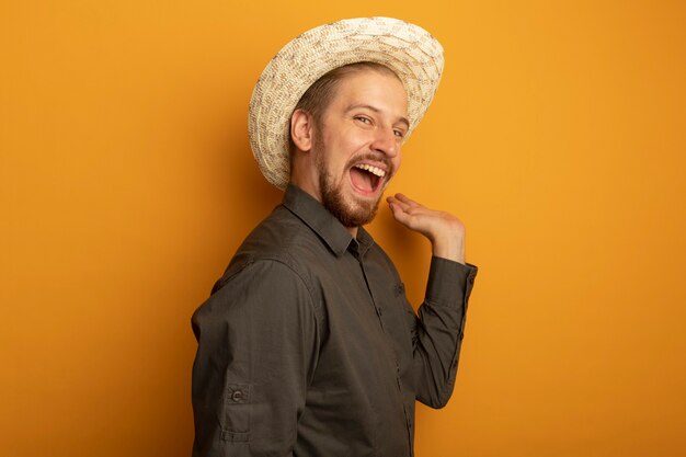 Jeune bel homme en chemise grise et chapeau d'été heureux et excité faisant des gestes avec la main