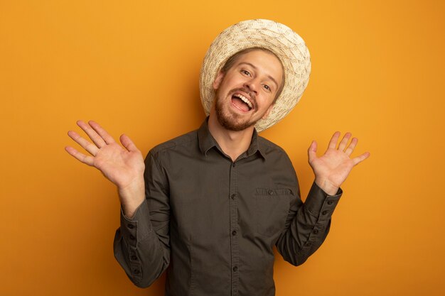 Jeune bel homme en chemise grise et chapeau d'été souriant avec un visage heureux avec les bras levés