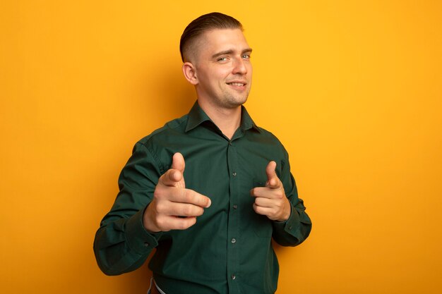 Jeune bel homme en chemise verte pointant heureux et positif avec les doigts à la caméra en souriant