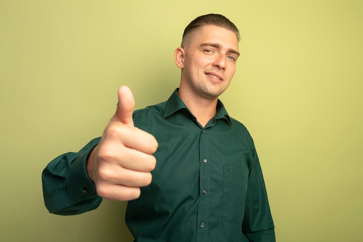 Photo gratuit jeune bel homme en chemise verte souriant avec visage heureux montrant les pouces vers le haut