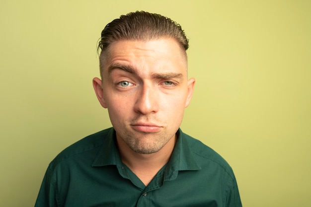 Jeune bel homme en chemise verte avec un sourire sceptique