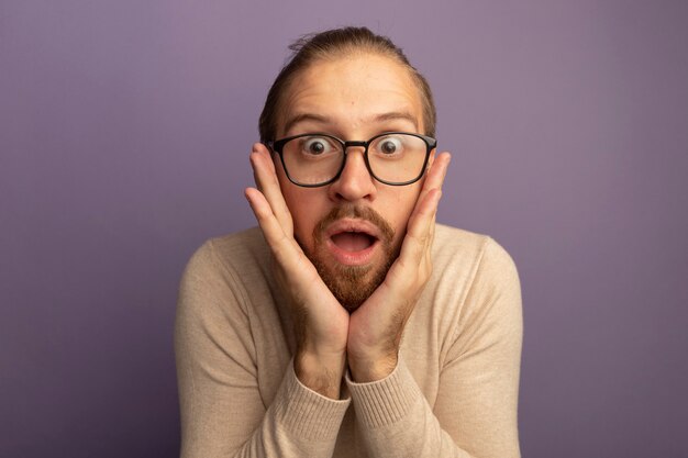 Jeune bel homme en col roulé beige et lunettes surpris et étonné