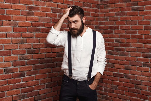 Jeune bel homme corrigeant la coiffure sur le mur de briques.