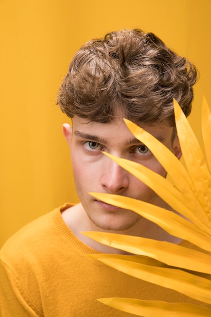 Jeune bel homme derrière une feuille de palmier dans une scène jaune