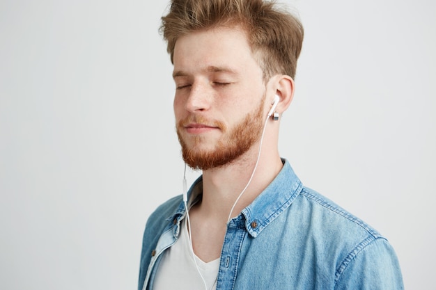 Jeune bel homme écoutant de la musique en streaming dans les écouteurs avec les yeux fermés appréciant.