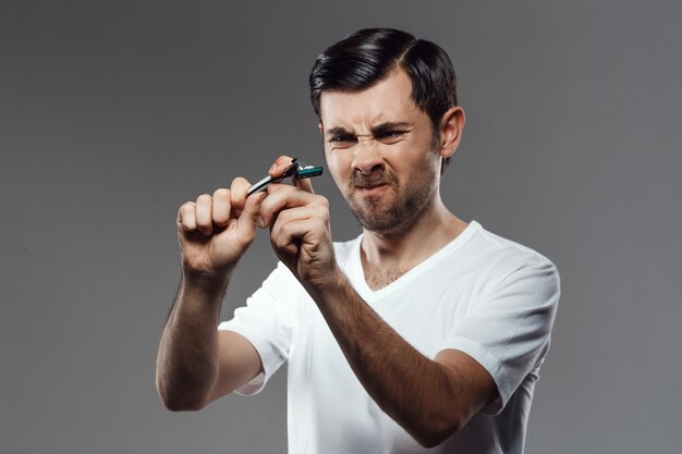 Jeune bel homme essayant de briser le rasoir sur le mur gris