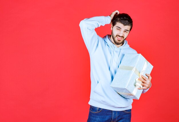 Jeune bel homme étreignant la boîte-cadeau emballée et a mis sa main à sa tête