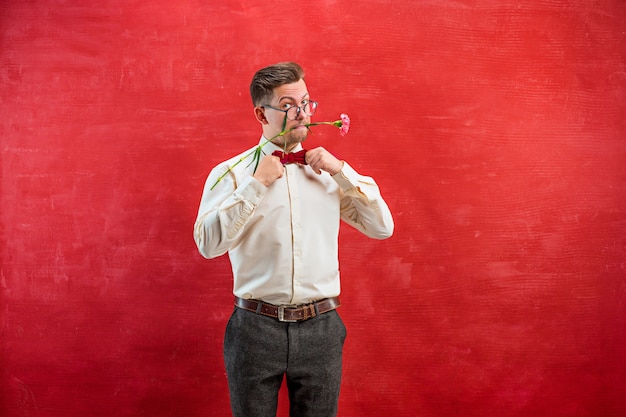 Jeune bel homme avec des fleurs sur studio rouge