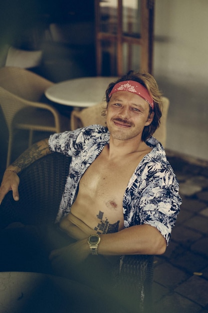 Photo gratuite jeune bel homme hippie dans un bandana rouge, avec un torse nu dans un café à bali. heureux homme souriant