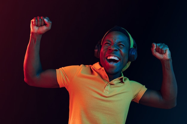 Le jeune bel homme hipster heureux écoute de la musique avec des écouteurs au studio noir