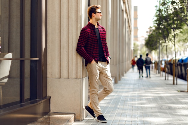 Jeune bel homme hipster posant sur la rue européenne, couleurs chaudes et ensoleillées aux tons chauds, vêtements à la mode décontractés, ambiance de voyage.