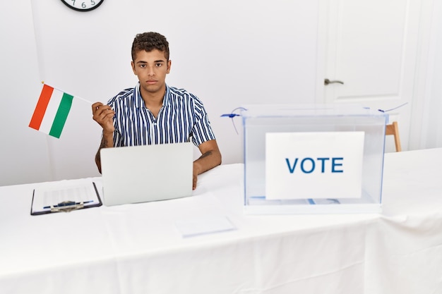 Photo gratuite jeune bel homme hispanique à l'élection de la campagne politique tenant l'attitude de pensée du drapeau hongrois et l'expression sobre à la confiance en soi