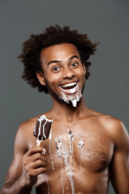 Jeune bel homme mangeant de la glace sur un mur gris