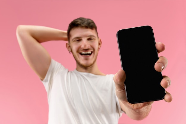 Jeune bel homme montrant l'écran du smartphone isolé sur fond rose en état de choc avec une surprise