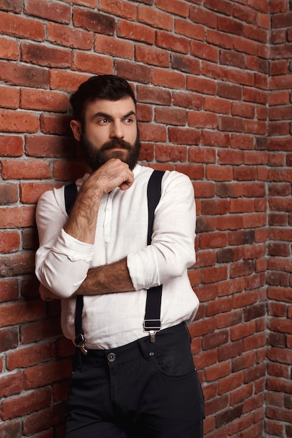 Jeune bel homme pensant posant sur le mur de briques.