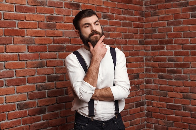 Jeune bel homme pensant posant sur le mur de briques.