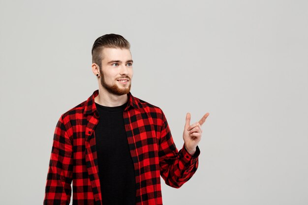 Jeune bel homme pointant le doigt sur le côté sur le mur gris.