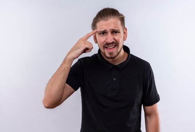 Jeune bel homme en polo noir à la recherche de temple de pointage inquiet et confus debout sur fond blanc